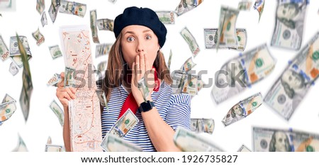 Young beautiful blonde woman wearing french beret holding city map covering mouth with hand, shocked and afraid for mistake. surprised expression
