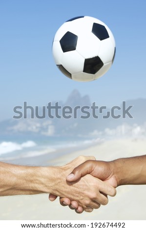 Brazilian interracial hands handshake in front of football above Two Brothers Mountain Ipanema Beach Rio de Janeiro Brazil