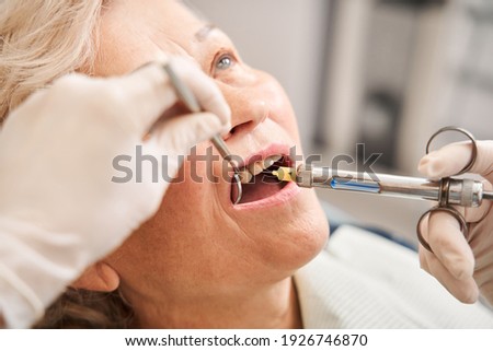 Senior woman at dentist office, getting local anesthesia injection into gums. Cropped view of the dentist numbing gums for dental work. Dental care concept