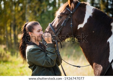 Cute girl talking with her horse after a joint walk in the background of the forest.