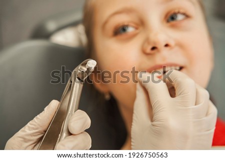 Preschooler child is at dentist office, medical forceps are extracting a milk tooth. Dental procedure, drilling, tooth extraction. Millennial lady doctor in uniform, protective mask and gloves with Royalty-Free Stock Photo #1926750563