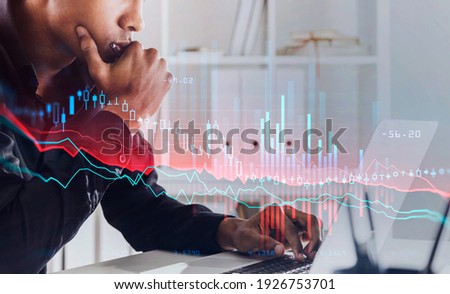Black man sitting with device in office room in suit, pensive looking and analysing. Stock statistics hud, candlesticks changes on foreground