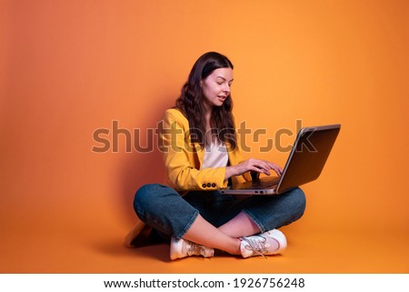 young woman in yellow is doing business on a laptop, a freelancer or a student is working remotely. Studio portrait on a yellow background