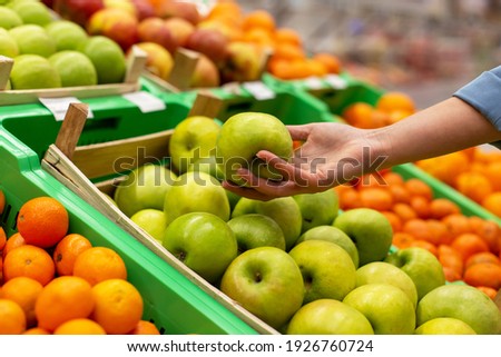 Picture of woman's hand holding an green apple in the supermarket. 