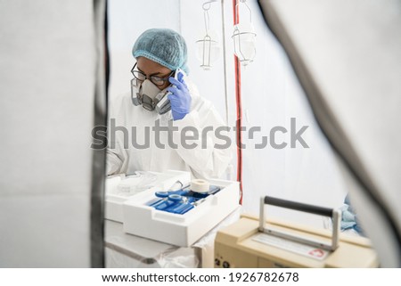 I listen you attentively. Attentive and tired young female doctor or nurse calling on smartphone and writing notes at the medical card of patient. Medicine, healthcare and pandemic concept