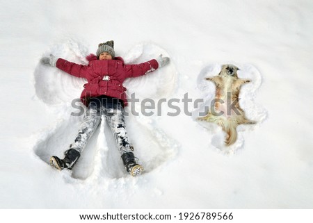 kid in the snow in winter makes a snow angel together with a dog