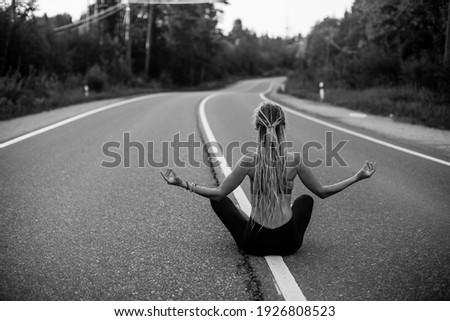 An yoga woman meditate sitting in the middle of the road. Black and white photo.