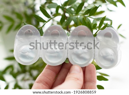plastic containers with contact lenses lie on the palm of a young girl, against a background of green leaves. Vision problems, alternative to glasses, eye comfort, increased cost of contact lenses