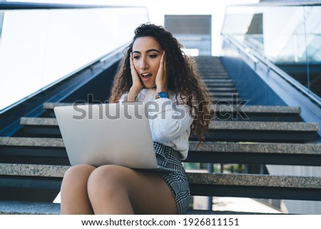 Amazed Turkish hipster girl impressed with received web newsletter during laptop programming at urban stairs, emotional female freelancer feeling shocked from wireless tariff for doing remote job