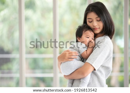 Young beautiful asian mother lifting and playing with her baby.