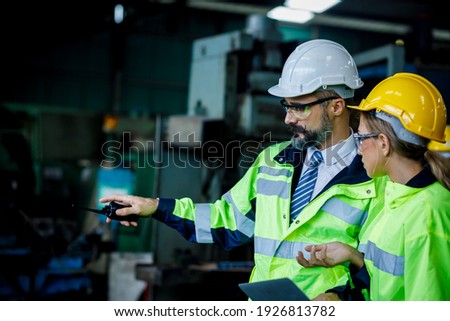 Male and female industrial engineer explaining the workplace. He is holding the walkie talkie on his hand while the pointing. Royalty-Free Stock Photo #1926813782