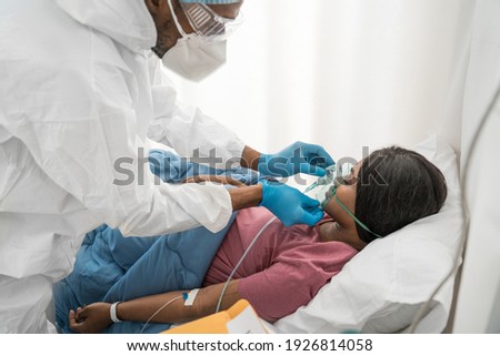Infected female patient lying on bed in hospital under care of medical worker with oxygen mask in quarantine room from coronavirus covid 19 disease. Stock photo