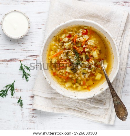 Thick hearty Pickle soup with vegetables (pickles, cucumbers, carrots, onions, potatoes, tomatoes) and pearl barley in a white plate on a wooden table. Rassolnik. Russian cuisine.  square picture