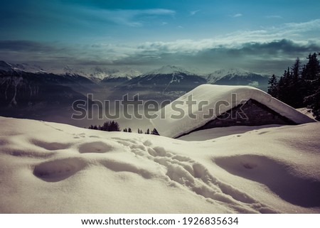 A small swiss chalet covered by snow with the Alpes in the background, shot in Verbier, Switzerland
