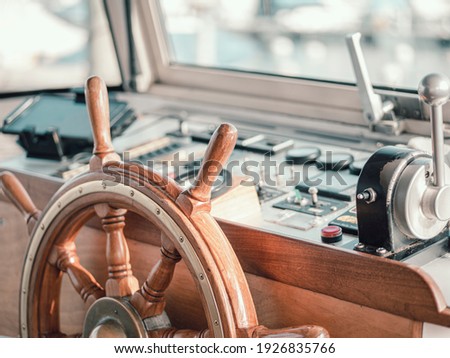Close up of the interior of a large motor boat. The steering wheel and motor controls can be seen and the boat harbor slurred through the glass boat window. Royalty-Free Stock Photo #1926835766