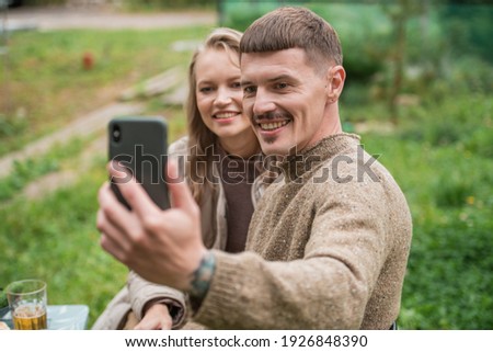 A young beautiful couple take photos of their new country house on a smartphone camera. Picnic in nature on the occasion of the purchase of real estate in the country