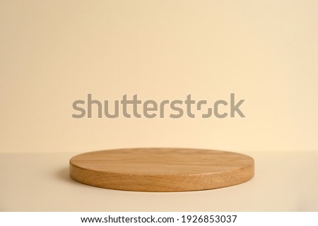 Round wooden podium on beige background for product presentation. Front view. Copy space.