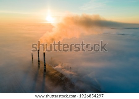 Aerial view of coal power plant high pipes with black smoke moving up polluting atmosphere at sunrise. Royalty-Free Stock Photo #1926854297