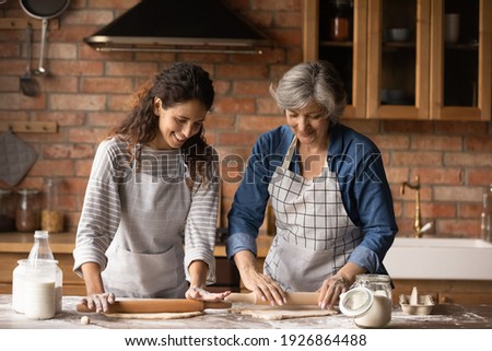 Happy Latino senior mother and grownup daughter make dough prepare sweet pie or pastries at home on weekend. Smiling Hispanic mature mom and adult girl cooking baking in kitchen. Hobby concept. Royalty-Free Stock Photo #1926864488