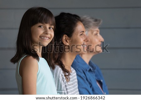 Portrait of happy little Hispanic 7s girl child look at camera smiling, mom and grandmother on background look in distance. Growing generation or small Latino kid with mother and senior grandparent. Royalty-Free Stock Photo #1926866342