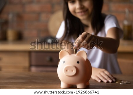 Crop close up of provident economical small girl kid put money into piggybank saving for future needs. Happy smart little 9s teen child make donation contribution in piggy bank. Investment concept. Royalty-Free Stock Photo #1926866741