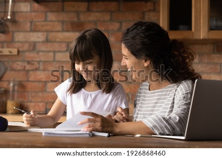 Happy caring young Latino mom do home work learn distant use computer with small biracial daughter. Smiling Hispanic mother help girl child with home task preparation. Online education concept. Royalty-Free Stock Photo #1926868460