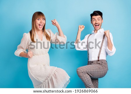 Photo of excited lucky young couple wear white outfit open mouth rising fists isolated blue color background