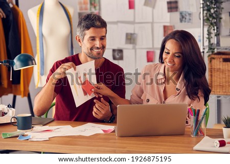 Male And Female Fashion Designers In Studio Presenting Designs During Video Call On Laptop