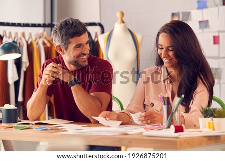 Male And Female Fashion Designers In Studio Working On Sketches And Designs At Desk