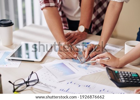Close-up image of business people pointing at document with statistics data when having meeting in office