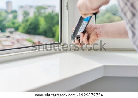 Artificial stone window sill, installation, technological process. Repair, construction of house, apartment. Worker with construction syringe fills seam between sill and window with silicone sealant Royalty-Free Stock Photo #1926879734