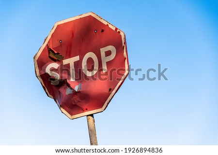 Damaged road sign stop covered with scratches and rusty. Rumpled road sign on a blue sky background. Stop sign with partly bent surface. Urban Grunge Background