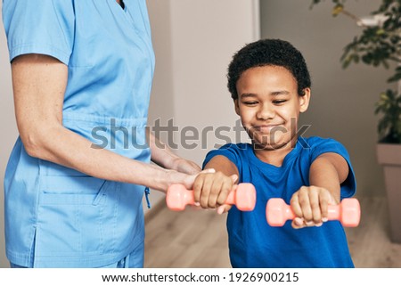 African American boy trains with physiotherapist using dumbbells at rehab center