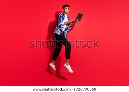 Full size profile side photo of young african man happy smile jump up use laptop isolated over red color background