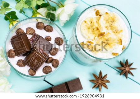 Romantic breakfast. Multi-layer dessert with yogurt, chocolate corn balls and slices of milk chocolate, banana dessert with cookies in a glass glass on a blue (mint) background. Top view.