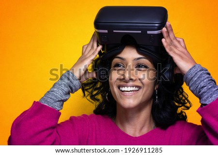 Beautiful young indian woman uses Vr glassess for augmented reality  - Pretty Sri Lanka girl uses technologic goggles posing with a yellow bright background
