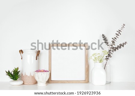 Mock up square wood frame with home decor, plants and flowers. White shelf against a white wall. Copy space.