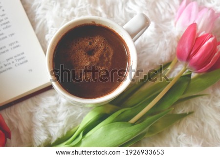 Book, coffee and tulips on a white furry carpet