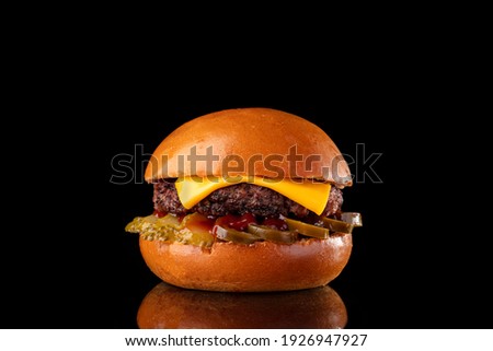 Classical cheeseburger isolated on black background. A Tasty burger sandwich with sliced pickled cucumbers, spicy jalapeno peppers, appetizing beef cutlet and melted cheese in crusty bun. Fast food