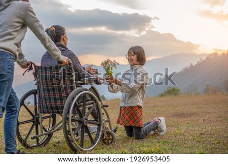 disabled handicapped woman sitting on her wheelchair with her daughter and care helper at sunset