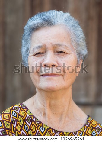 Portrait of a senior woman with short gray hair, smiling and looking at the camera while standing outdoors with wooden wall background. Space for text. Concept of aged people and healthcare.