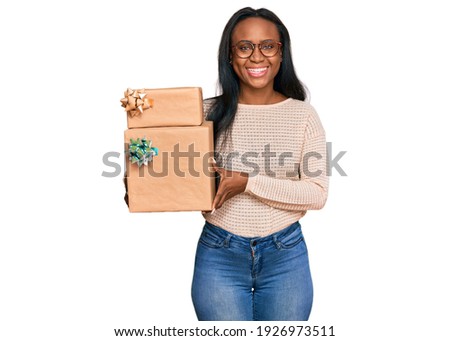 Young black woman holding gifts looking positive and happy standing and smiling with a confident smile showing teeth 