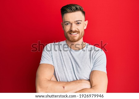 Young redhead man wearing casual grey t shirt happy face smiling with crossed arms looking at the camera. positive person. 
