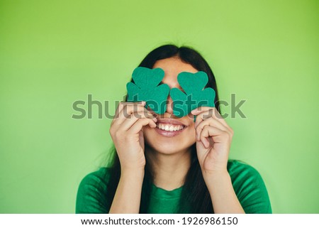 Modern girl holding a shamrock on an isolated green background. Happy St Patrick's day.
