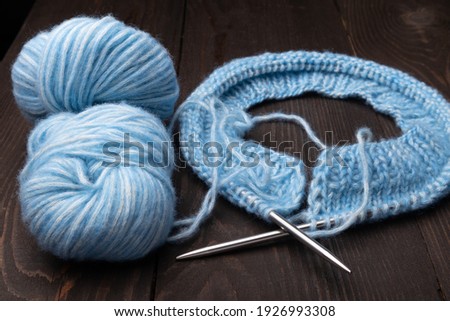 knitting needles, blue yarn and skeins on a dark wooden background