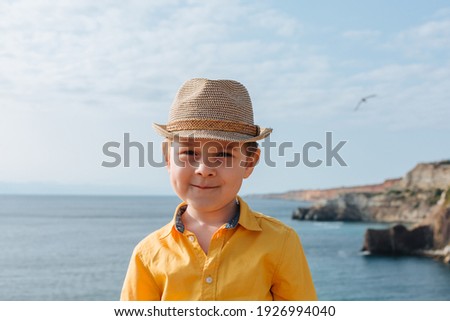 portrait of a boy 4-7 against the background of mountains and the sea. He is wearing a yellow shirt and hat. Smiles.