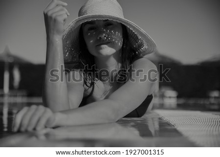 Seductive young woman relaxing in the sun wearing a straw hat on a sunny day. Resort and summer concept. Black and white photo.