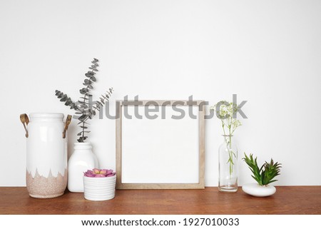 Mock up square wood frame with home decor, plants and flowers. Wooden shelf against a white wall. Copy space.