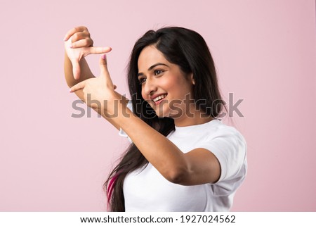Beautiful Indian woman making a hand frame over pink background, composing picture ideas