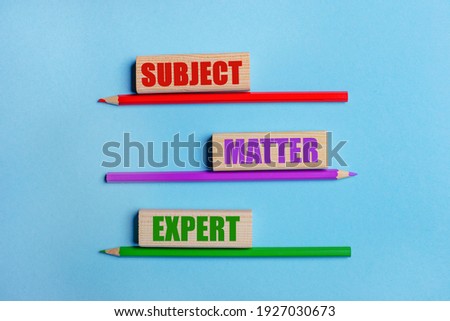 On a blue background, three colored pencils, three wooden blocks with text SUBJECT MATTER EXPERT